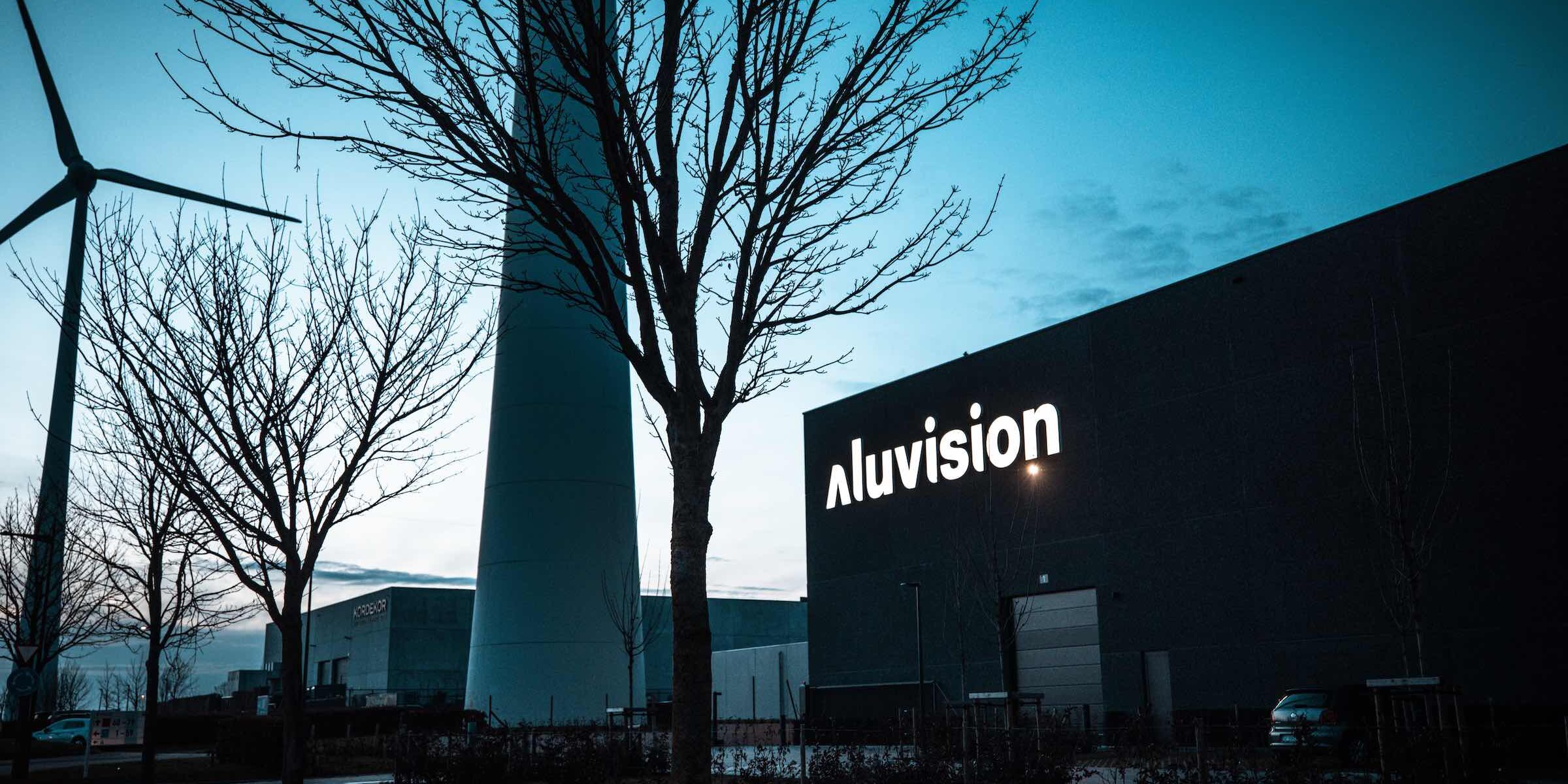 Außenansicht des Aluvision Gebäudes bei Abendlicht mit beleuchtetem Logo.