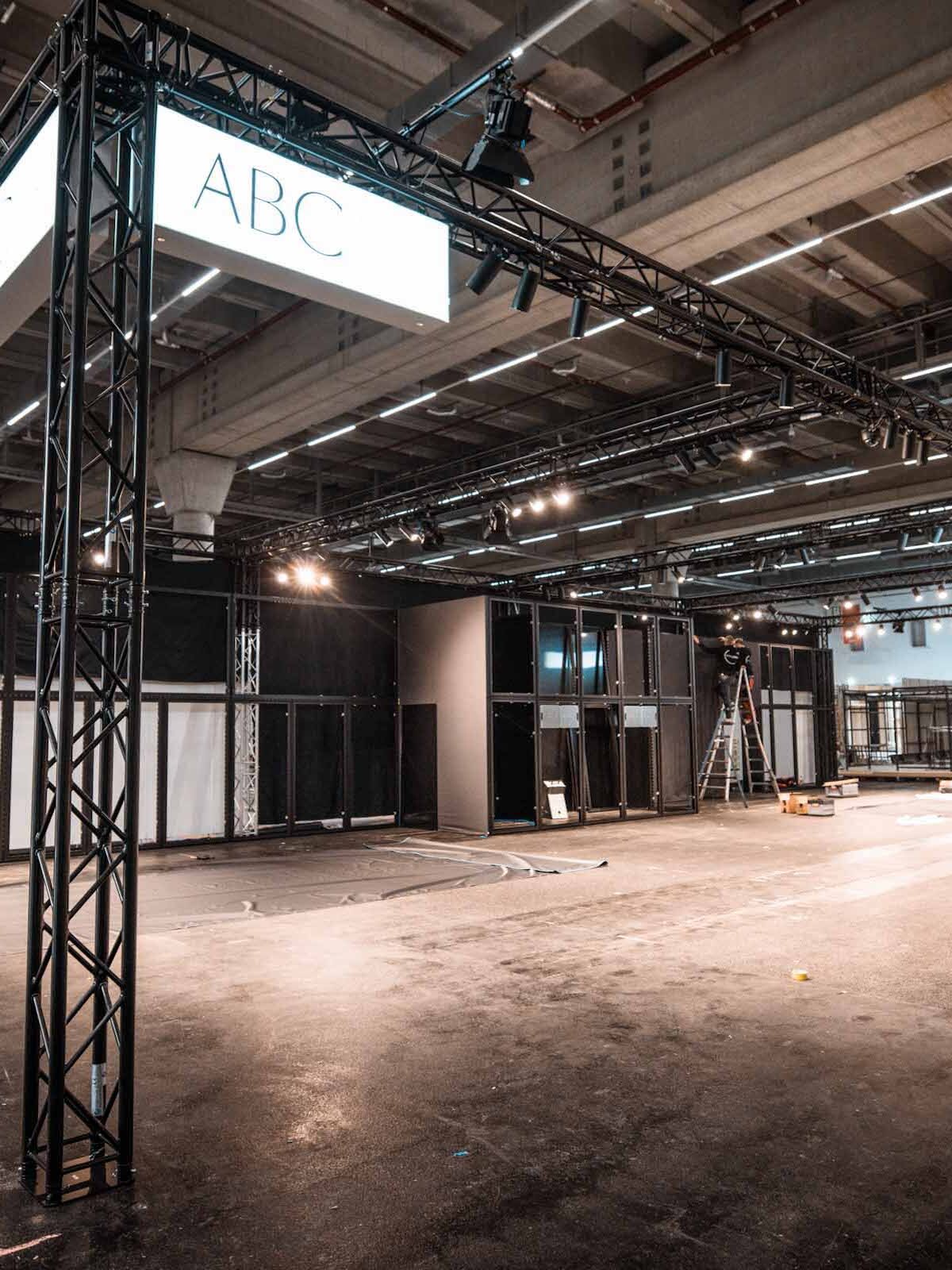 Gro&szlig;er Messestand-Rohbau mit schwarzer Traversenkonstruktion und beleuchtetem &bdquo;ABC&ldquo;-H&auml;ngeschild in der Messehalle.