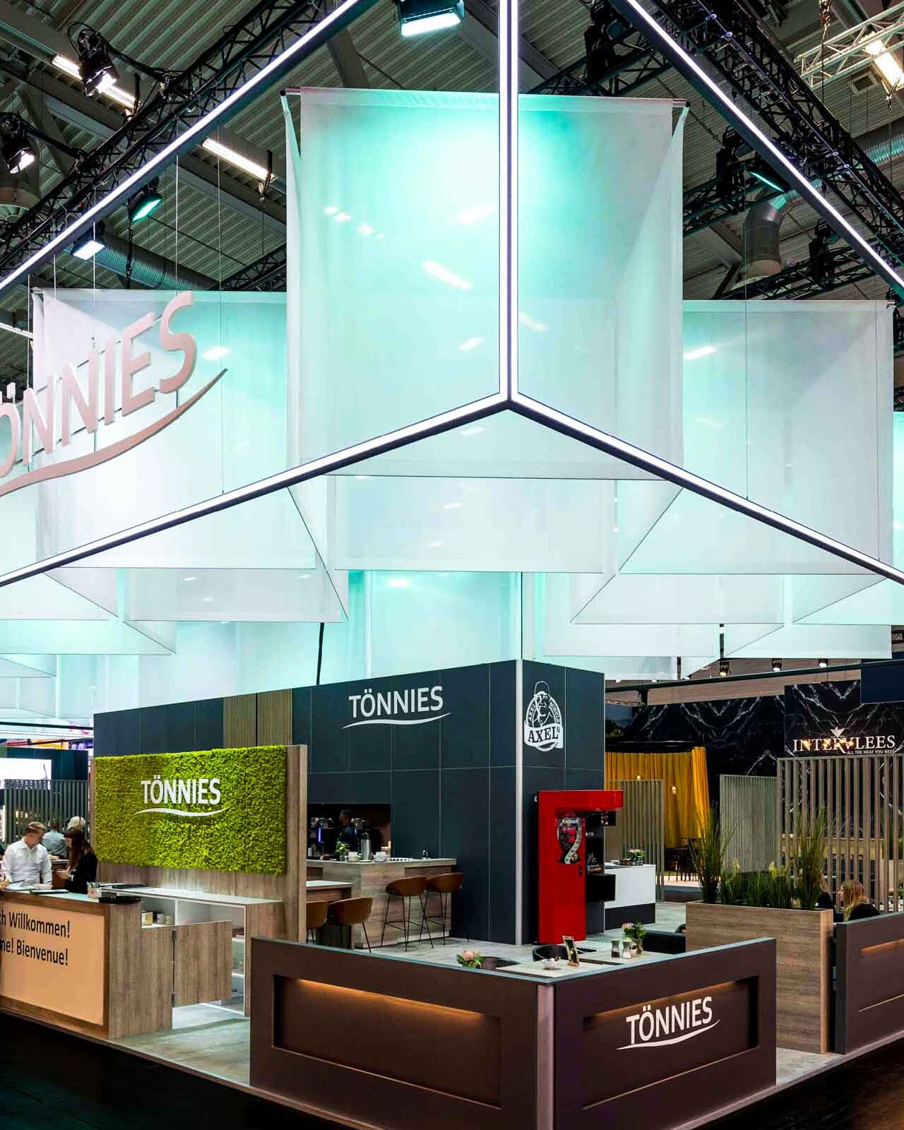 önnies Messestand mit großer, beleuchteter Deckenstruktur, transparenten Hängeflächen und Empfangsbereichen.