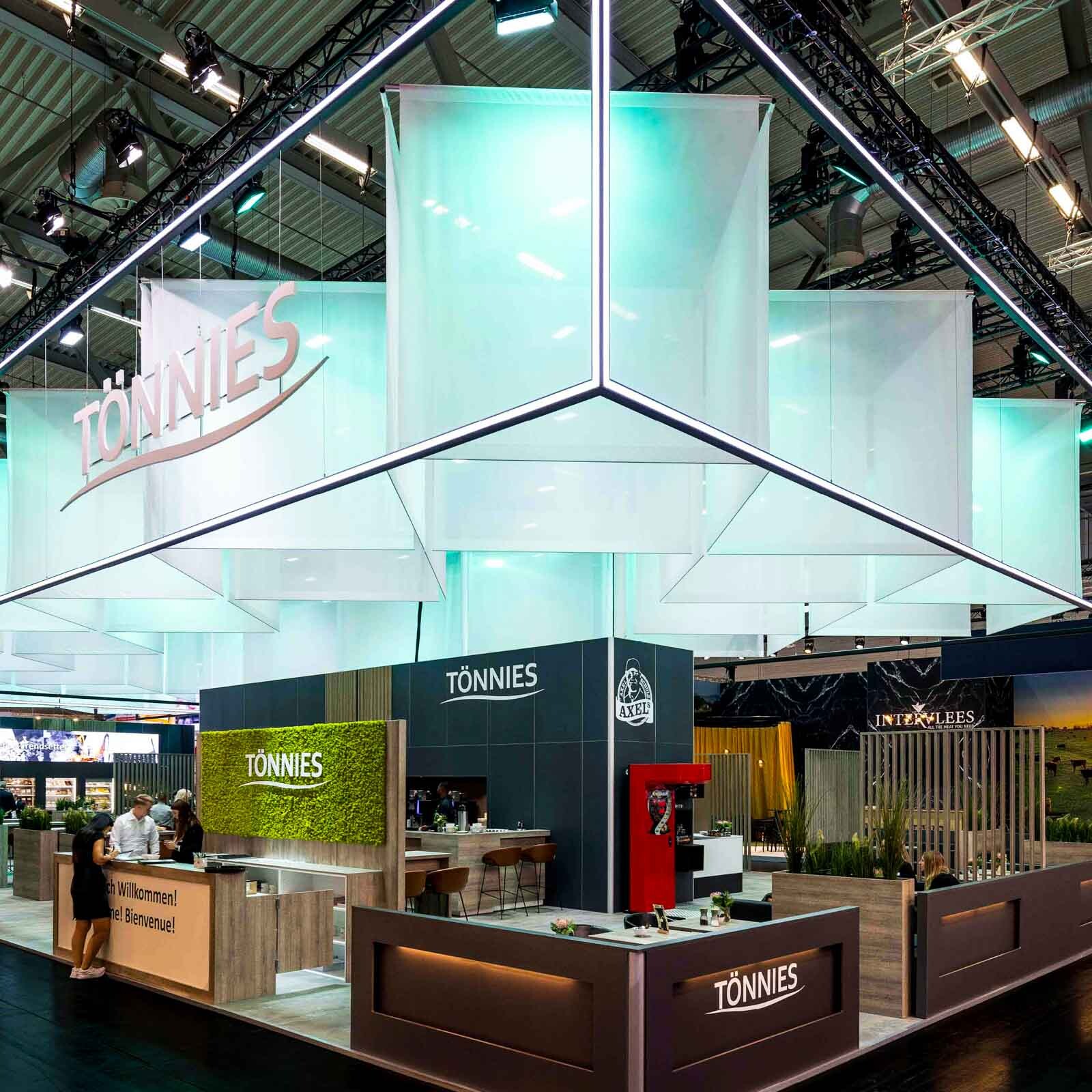 önnies Messestand mit großer, beleuchteter Deckenstruktur, transparenten Hängeflächen und Empfangsbereichen.