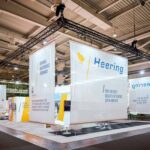 Großer Messestand mit Traversensystem, Bannern und Beleuchtung in Messehalle für professionellen Messebau