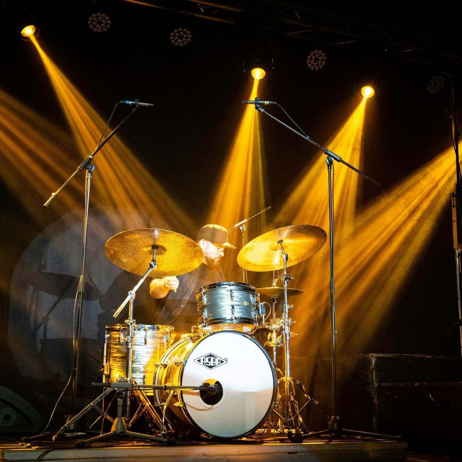 Schlagzeug auf Bühne mit gelber Konzertbeleuchtung und professioneller Lichttechnik bei einem Live-Event